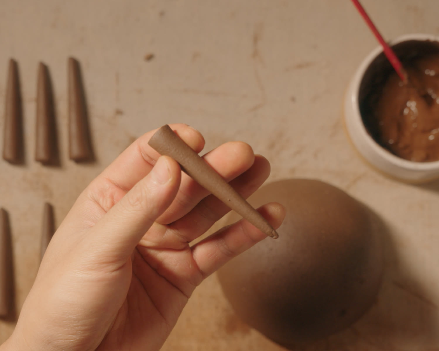 Hand rolling a clay spike beside a row of finished spikes and the half sphere bowl