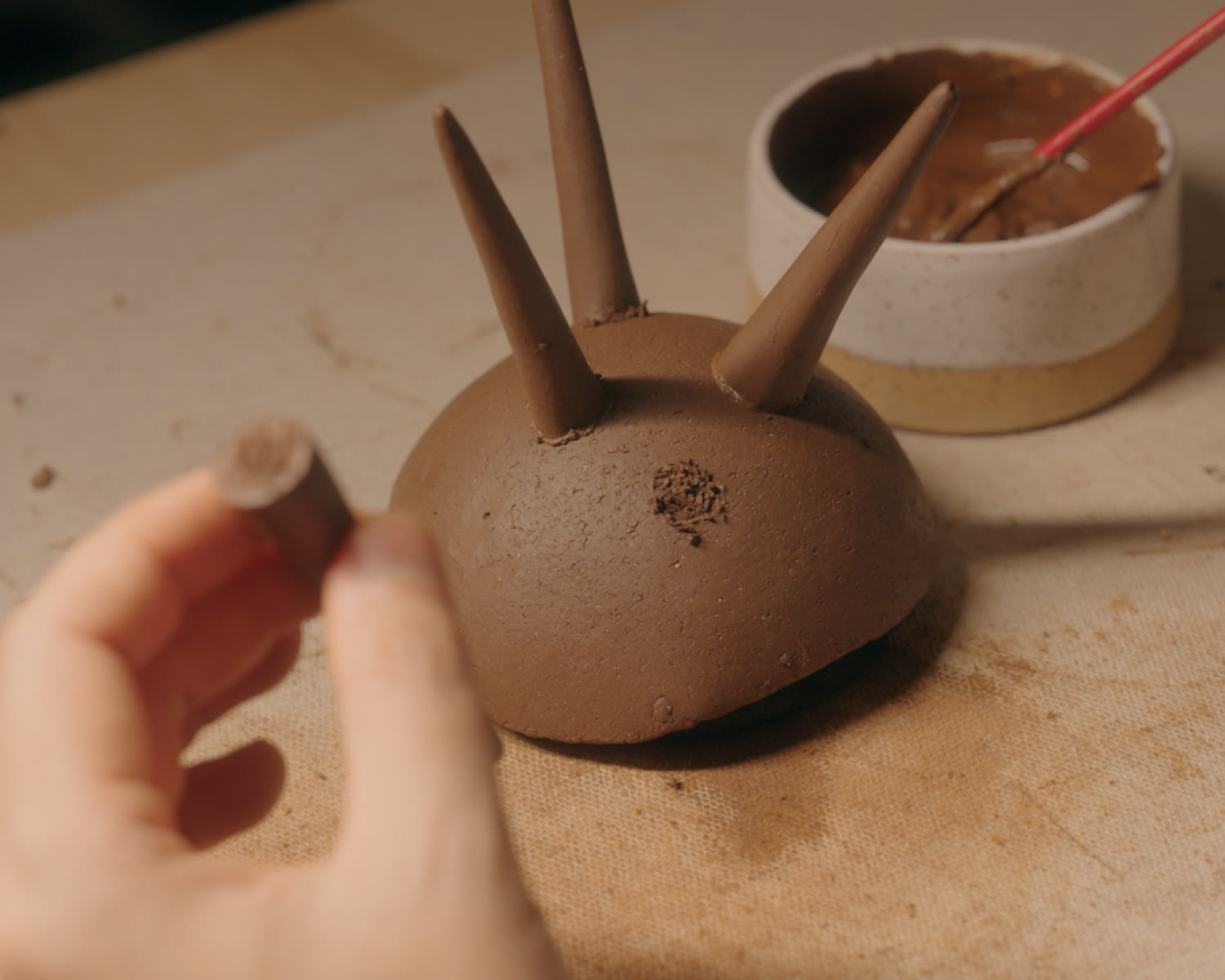 Scoring a spike before attaching it to the bowl, with a bowl of slip alongside