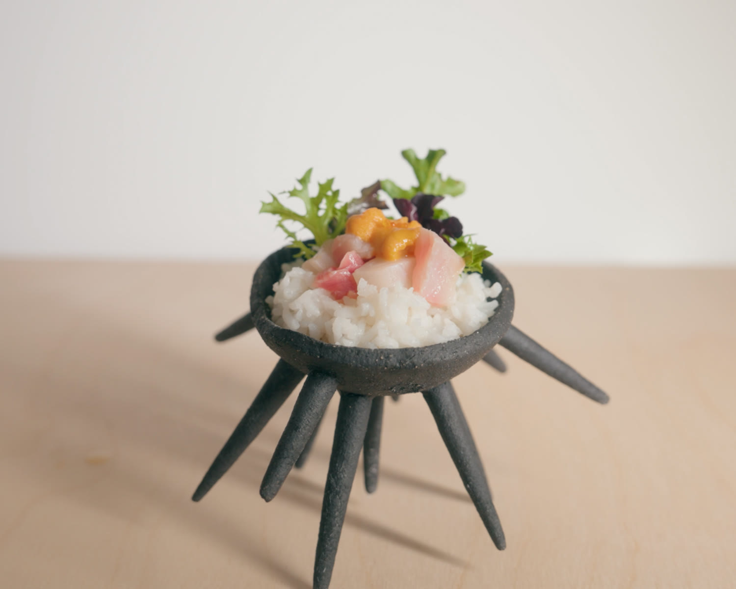 The bowl holding a chirashi of rice, uni, sashimi, and greens